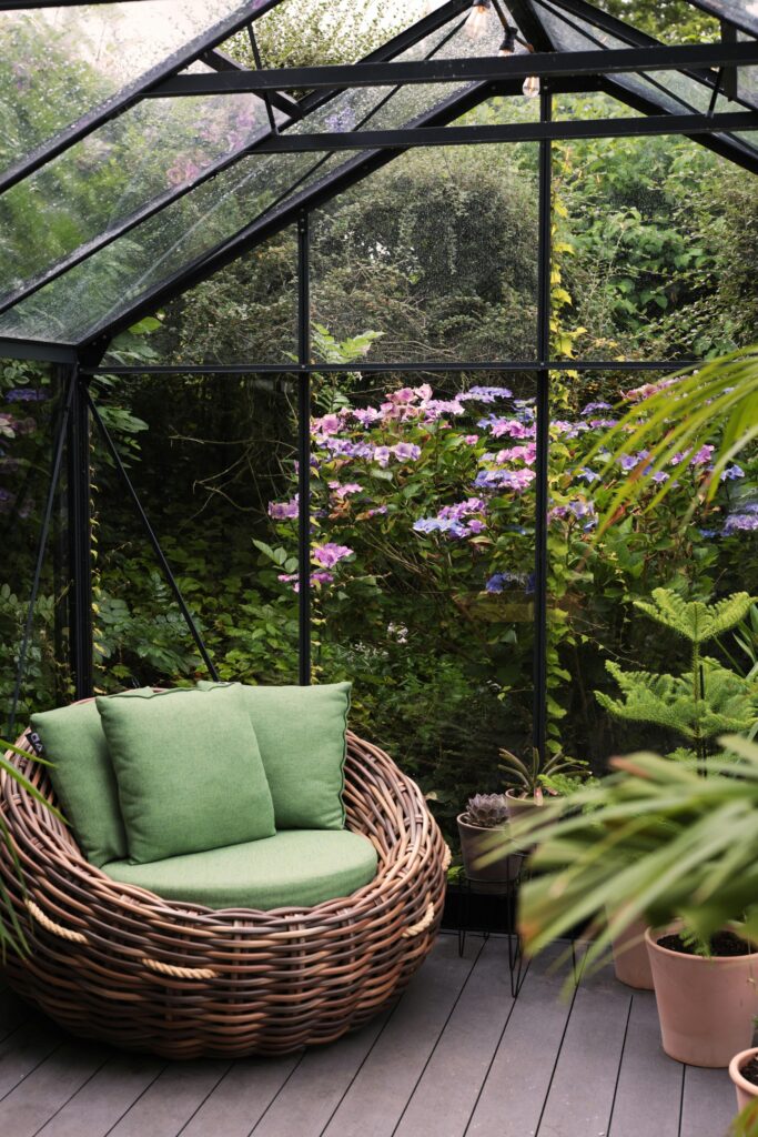 Relax in a wicker armchair amidst vibrant plants and flowers in a greenhouse sanctuary.