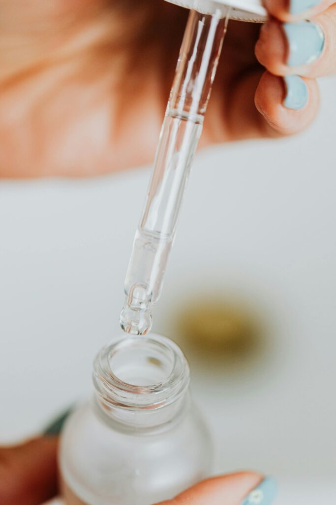 Detailed close-up of a dropper dispensing liquid into a glass serum bottle for skincare routine.
