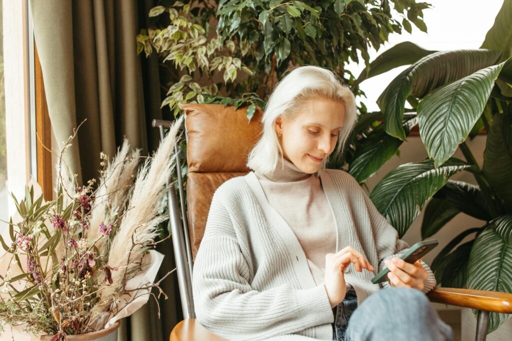 A woman enjoying a relaxed moment indoors with houseplants and a smartphone in hand.