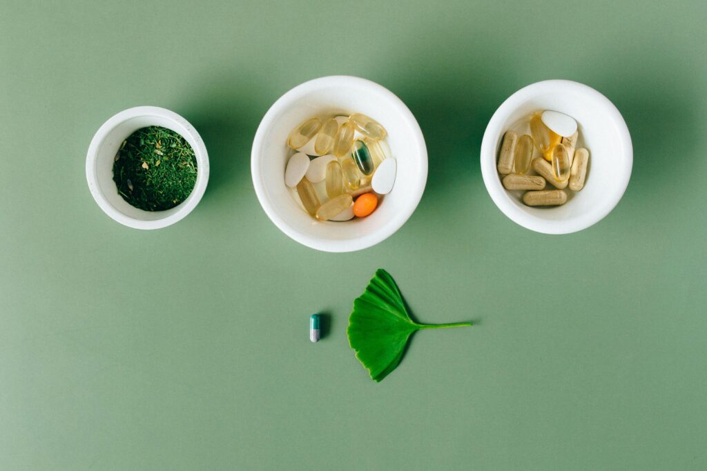 pexels photo 7615558 7615558 Flatlay of capsules and herbs in ceramic bowls on green surface.