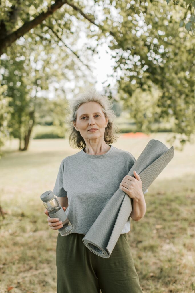 pexels photo 8940487 8940487 Elderly woman smiling outdoors holding a yoga mat and water bottle, promoting wellness and healthy living.